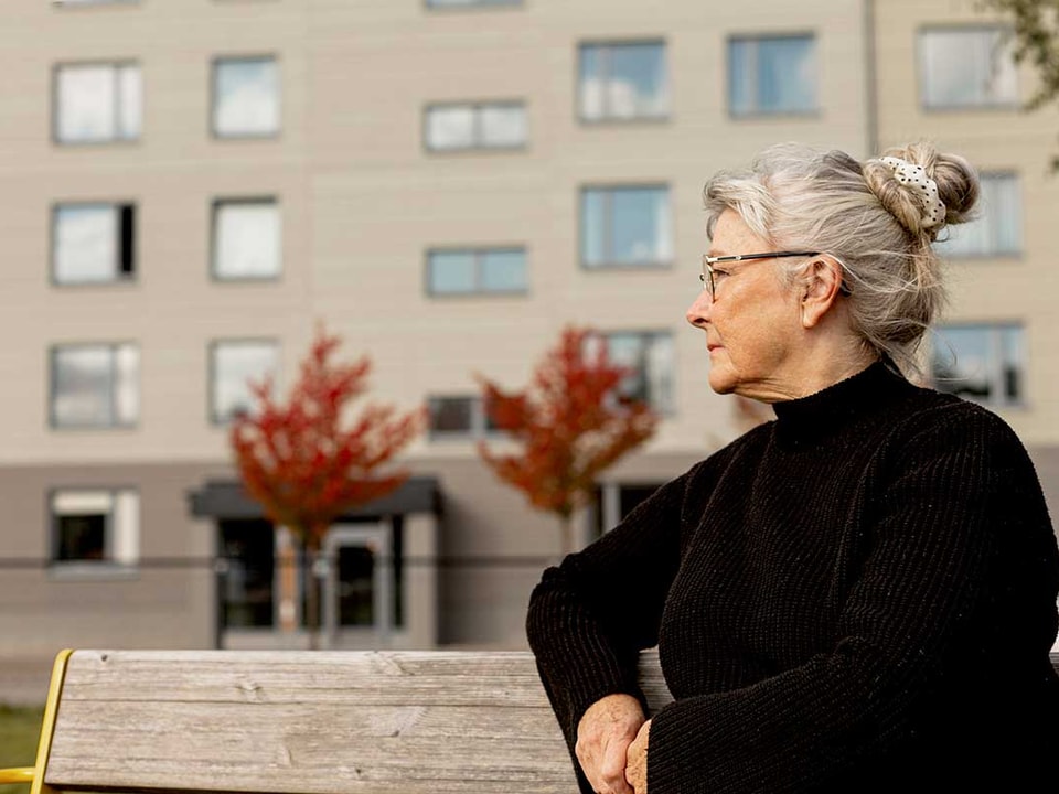Eldre kvinne sitter på en benk utenfor en boligblokk, til illustrasjon for økonomi for eldre
