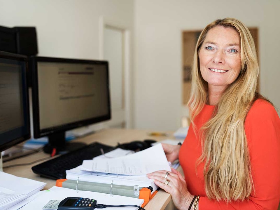 Kvinne sitter ved en pult med en stor bok med dokumenter for å få kontroll på økonomien