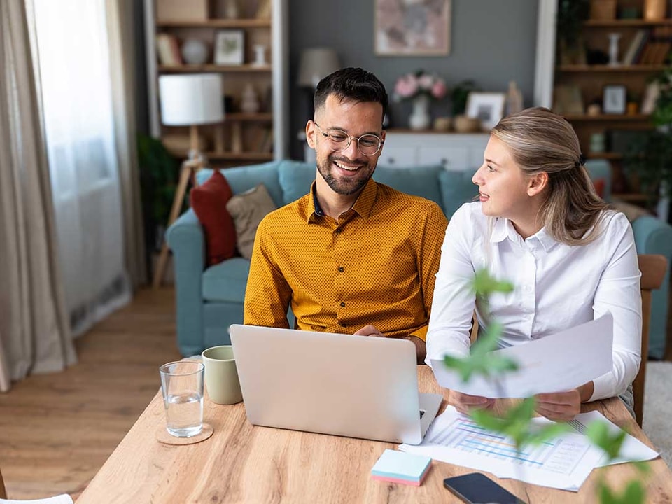 Par sitter ved spisebordet og ser på papirer og pc, til illustrasjon for hvordan spare 100.000 kr