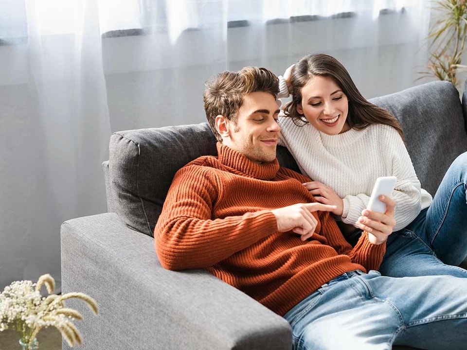 Par i sofa som ser på mobilen, til illustrasjon for få pengene til å vare lenger