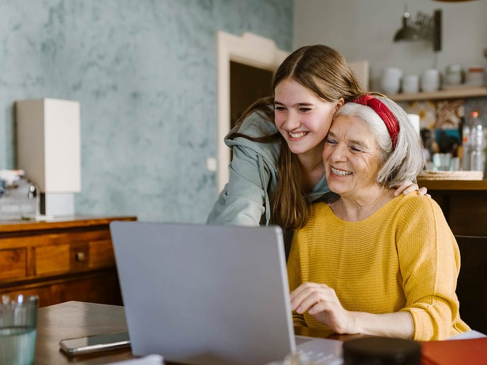 Jente klemmer eldre kvinne mens de ser på en dataskjerm, til illustrasjon for spare til barnebarn