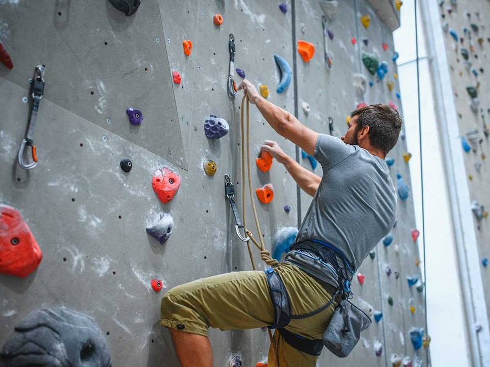 Mann klatrer i klatrevegg, til illustrasjon for bedriftskunder som er i lag og forening