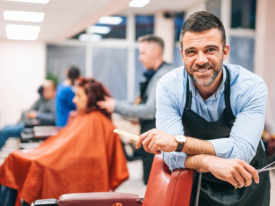 Frisør lener seg over frisørstol i sin egen bedrift, til illustrasjon for driftskonto