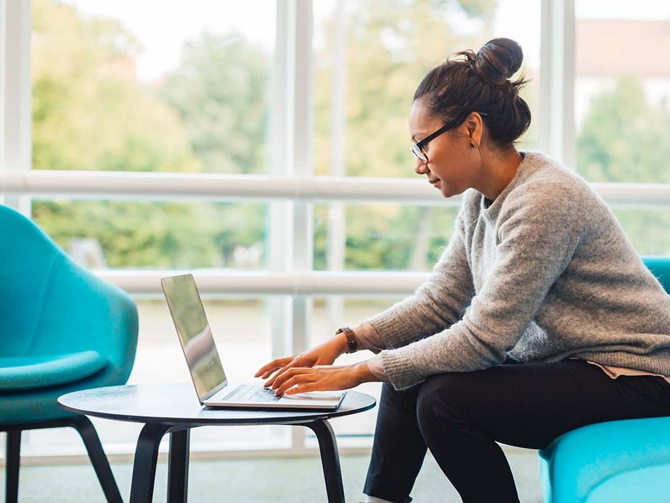 Dame sitter på en blå sofa og jobber på en laptop, til illustrasjon for kredittpolicy