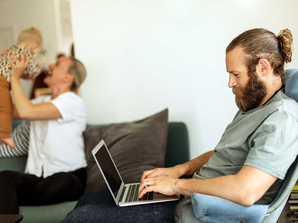 Mann i godstolen jobber på PC med familien i bakgrunnen, illustrasjon til veileder om hvordan endre beløpsgrense nettbank