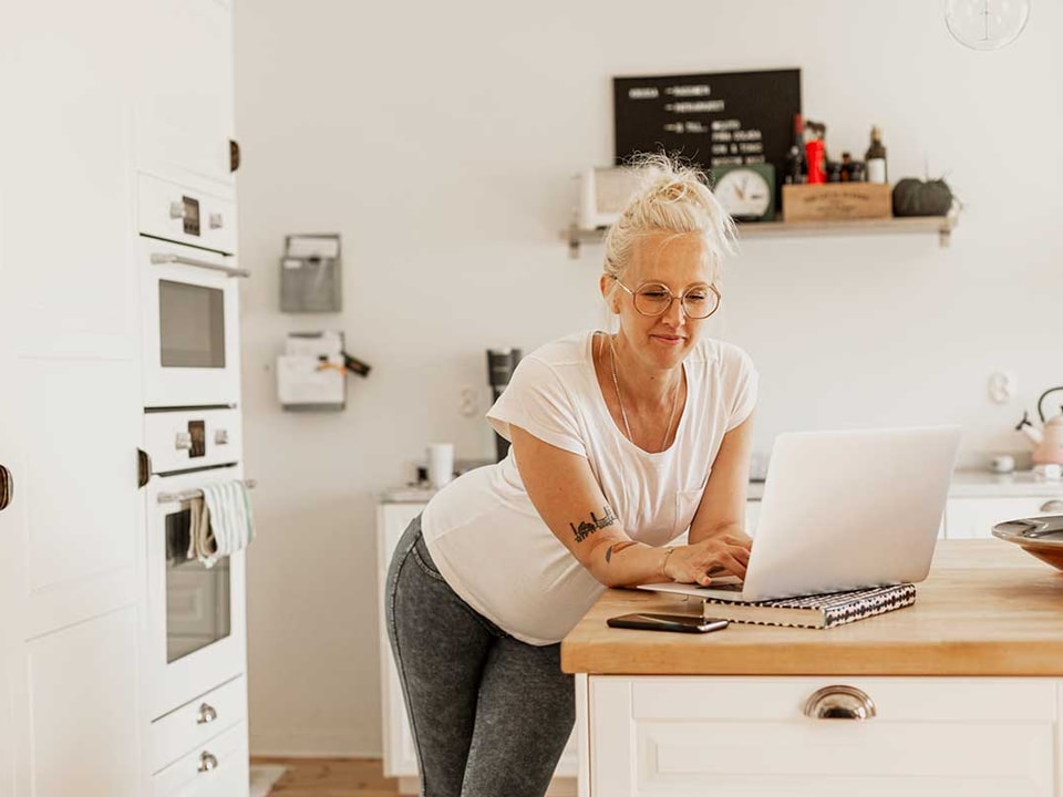 Dame med laptop står ved kjøkkenbenken, illustrasjon til veileder om hvordan legge til disponent på konto