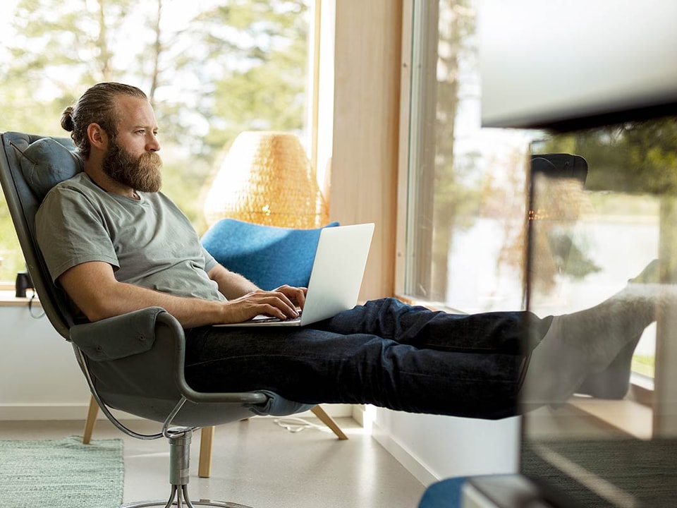 Kvinne sitter på sofaen med datamaskin i fanget, til illustrasjon for sikkerhet på nett