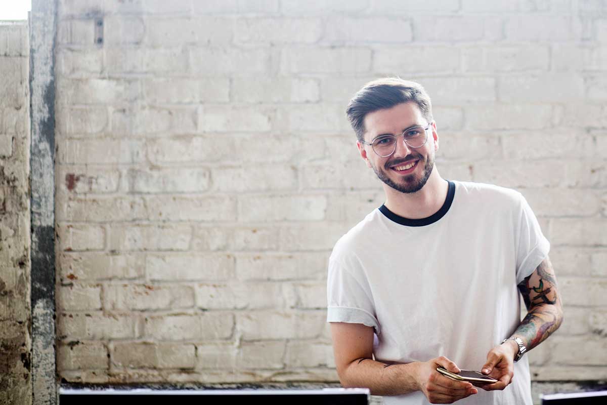 Ung mann fremfor murvegg holder en notatblokk, til illustrasjon for kjøpe første bolig