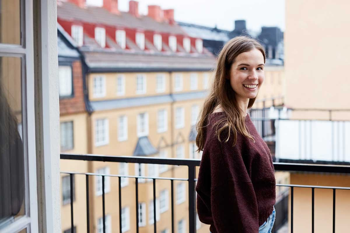 Ung jente står på en balkong og smiler, til illustrasjon for førstegangskjøp av bolig