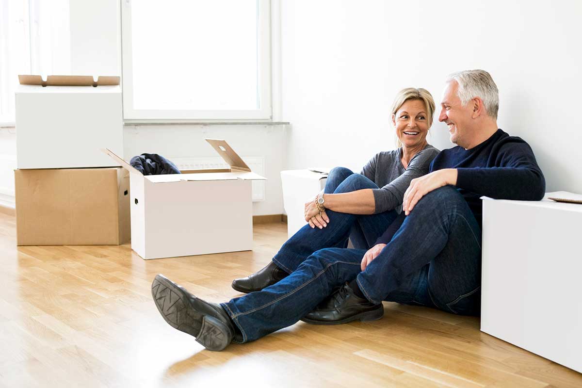 Par sitter på gulvet med flytteesker, til illustrasjon for å selge bolig