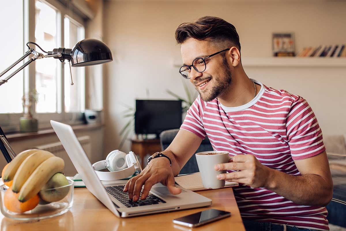 Mann sitter ved pulten med en kaffekopp i hånda og jobber på PC, til illustrasjon for hvordan beregne egenkapital