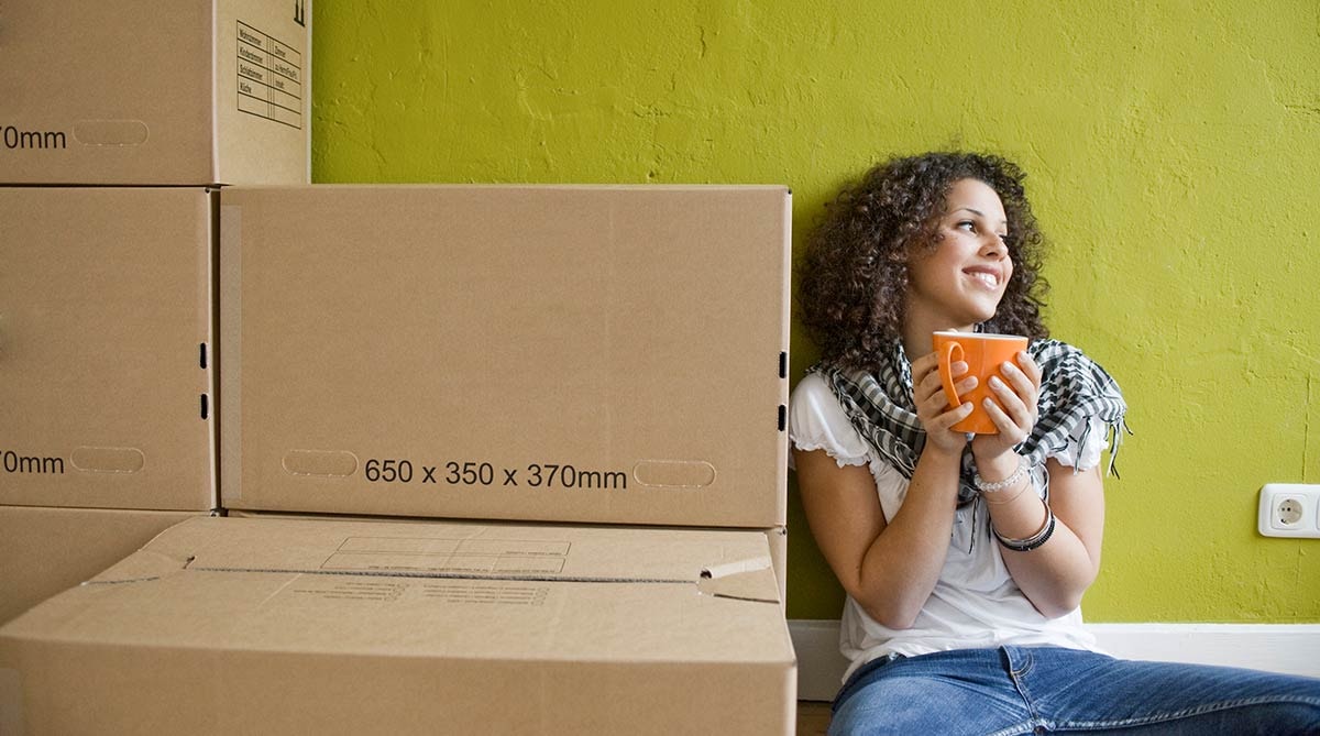 Dame sitter på gulvet og drikker kaffe med flyttekasser rundt seg, til illustrasjon for Finit deleie