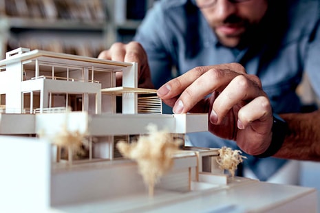 Mann leker med minivariant av et hus, til illustrasjon for å bygge på huset