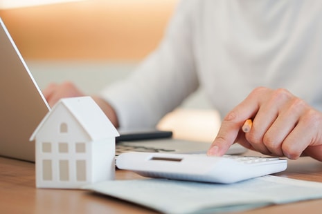 Dame sitter ved bord og skriver på kalkulator, til illustrasjon for refinansiere forbruksgjeld