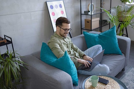 Mann sitter i sofa og jobber på PC, til illustrasjon for hvordan spare penger