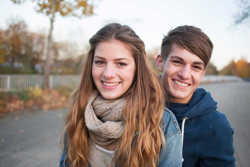Ung jente og gutt smiler, med løv i bakgrunnen, til illustrasjon for endelig myndig