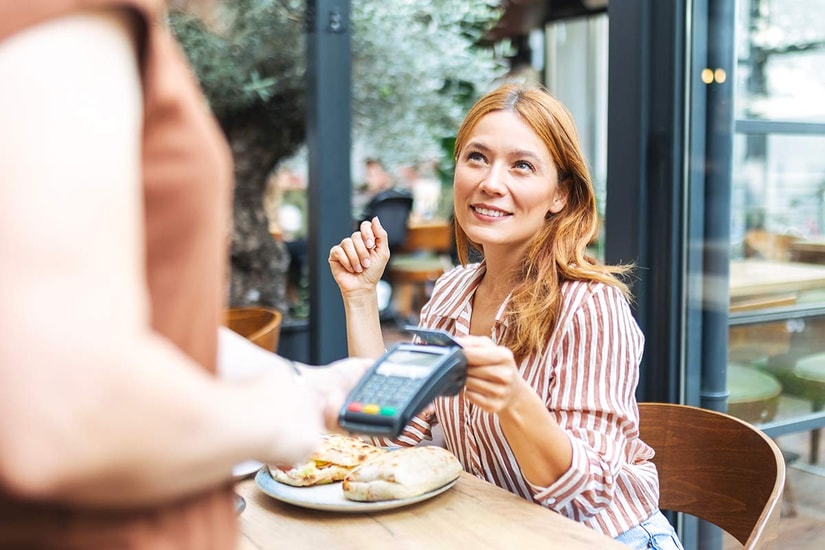 Dame på cafe tapper kort på terminal, til illustrasjon for bankkort