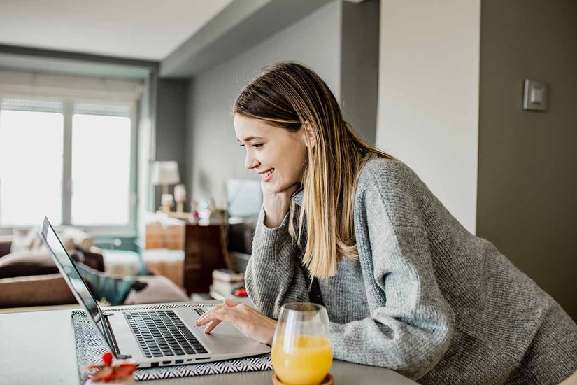 Ung kvinne lener seg over kjøkkenbenken og jobber på en PC, til illustrasjon for bytte bolig