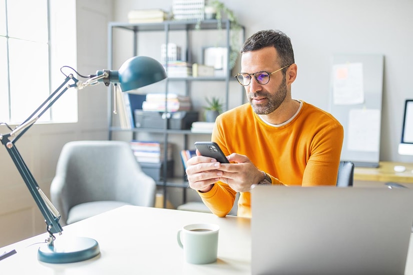 Mann i orange genser ser på mobilen, til illustrasjon for mine kort app