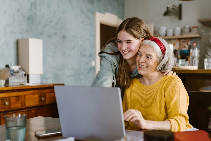 Jente klemmer eldre kvinne mens de ser på en dataskjerm, til illustrasjon for spare til barnebarn