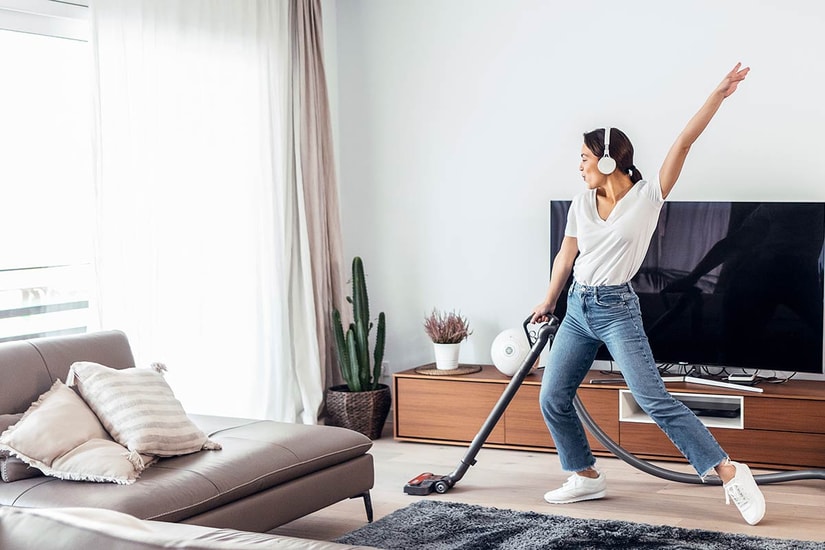 Ung jente danser mens hun hører på musikk og støvsuger boligen, til illustrasjon for BSU