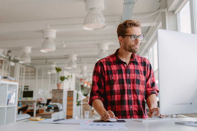 Mann i rutete skjorte ser på mac skjerm, til illustrasjon for bankkort for bedrift