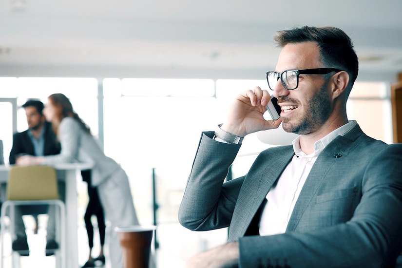 Mann med dress og briller snakker i mobil med kollegaer bak seg, til illustrasjon for NIBORkonto