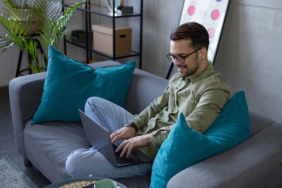 Mann sitter i en sofa og jobber på en PC, til illustrasjon for AvtaleGiro