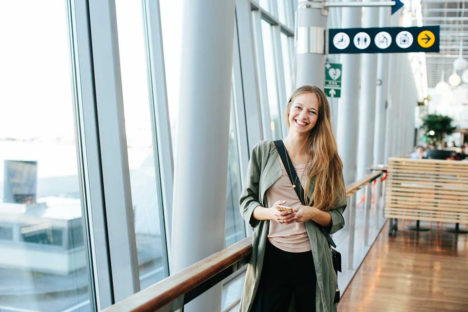 Jente står på flyplassen med mobilen i hånda, til illustrasjon for mobilbank
