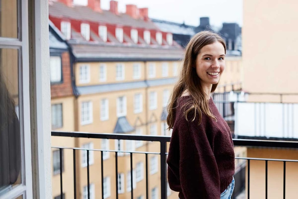 Ung jente står på en balkong og smiler, til illustrasjon for førstegangskjøp av bolig