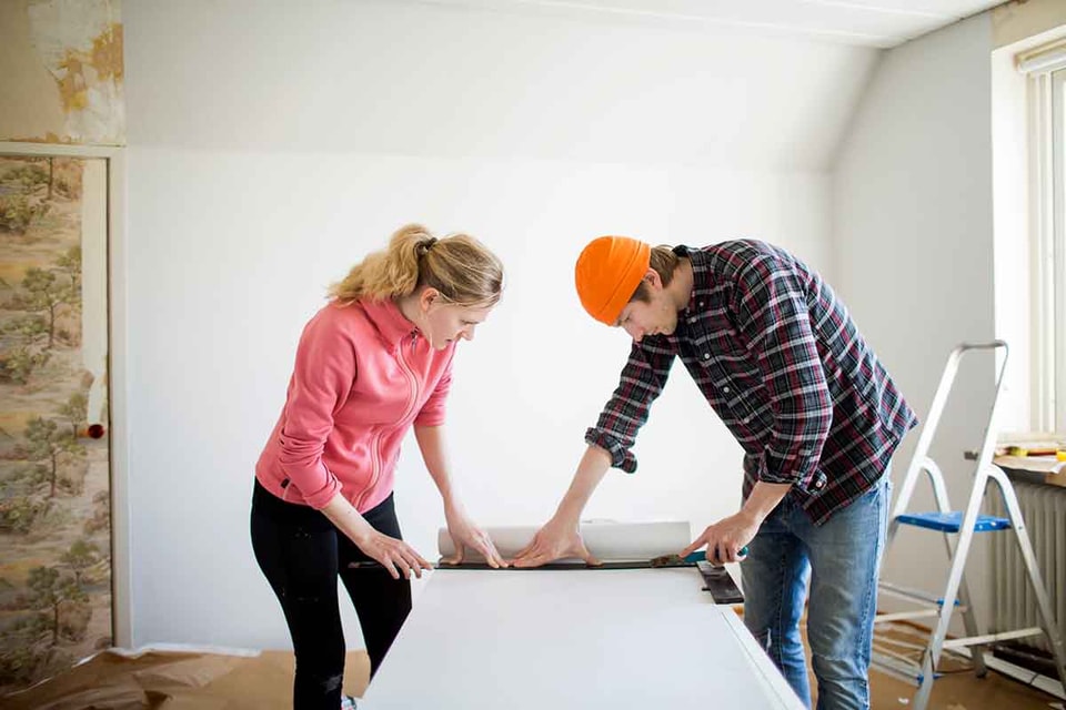 Dame og mann måler tapet mens de pusser opp, til illustrasjon for spare eller låne til oppussing