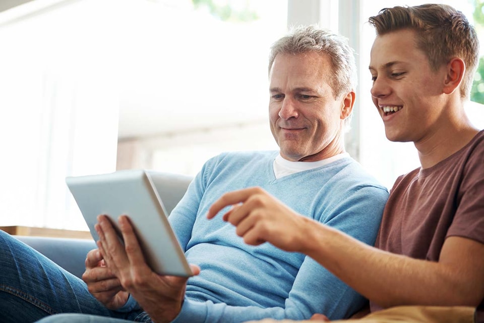Far og sønn sitter og ser på nettbrett