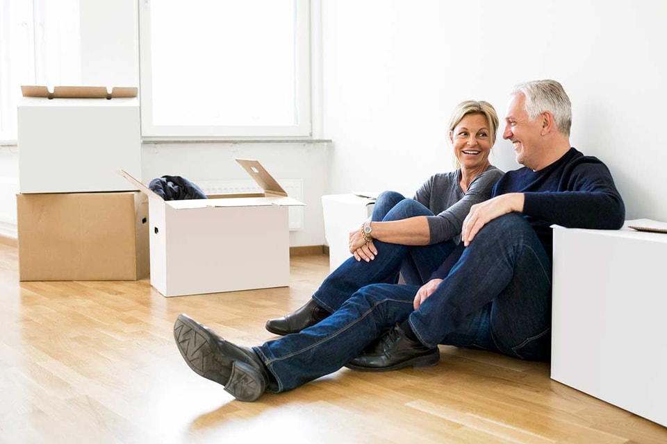 Par sitter på gulvet med flytteesker, til illustrasjon for å selge bolig