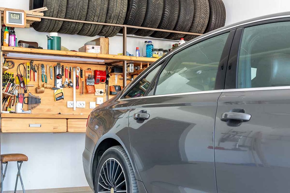 Bil er rygget inn i garasje som har lagringsplass for dekk og oppbevaring for verktøy, til illustrasjon for bygge garasje