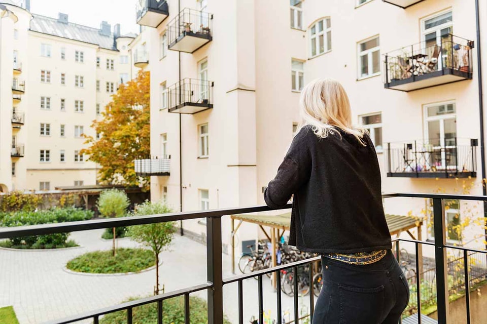 Dame på balkong ser utover bygård, til illustrasjon for selveier, andel og aksjeleilighet