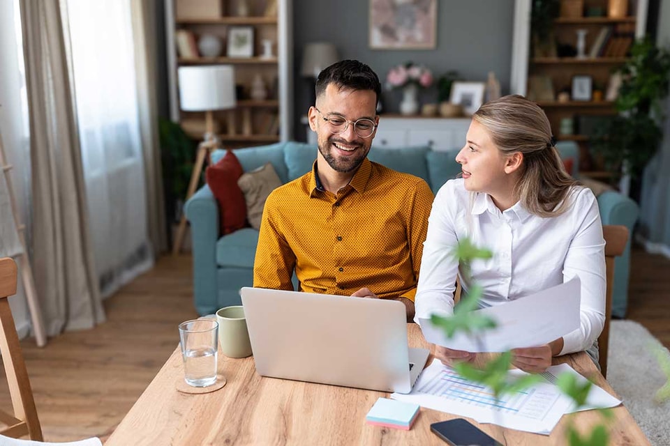 Par sitter ved spisebordet og ser på papirer og pc, til illustrasjon for hvordan spare 100.000 kr