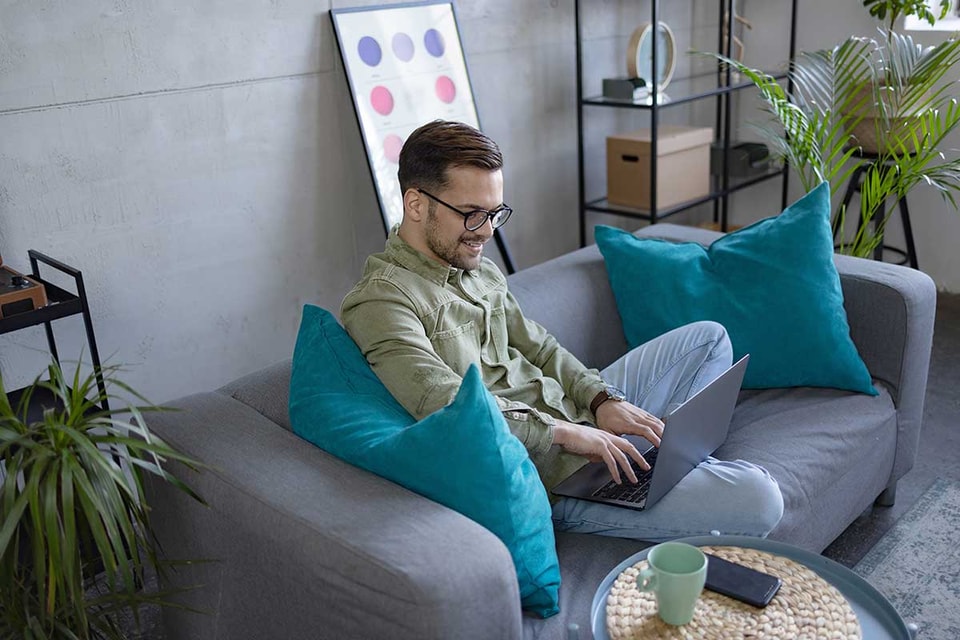 Mann sitter i sofa og jobber på PC, til illustrasjon for hvordan spare penger
