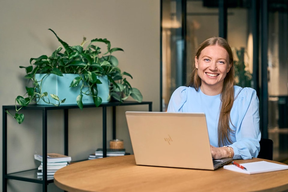 Kvinne sitter foran pc ved et rundt bord