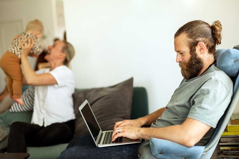 Mann i godstolen jobber på PC med familien i bakgrunnen, illustrasjon til veileder om hvordan endre beløpsgrense nettbank