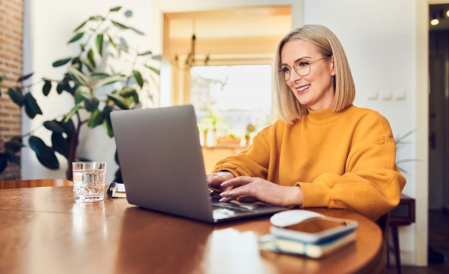 Dame i oransje grenser sitter ved spisebord og ser på datamaskin, til illustrasjon for betale til utlandet