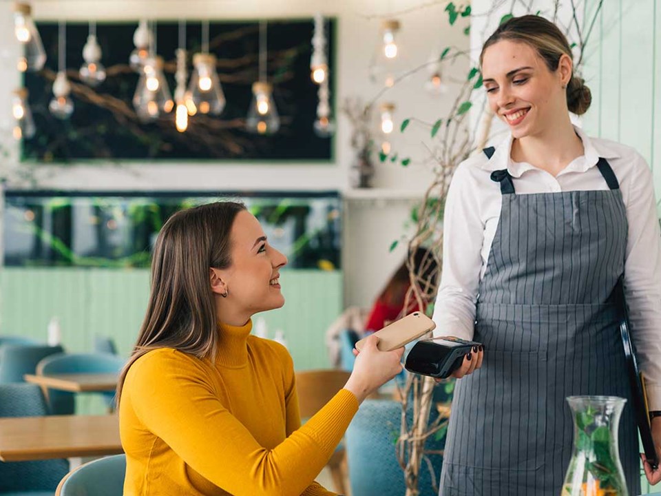 Dame sitter på kafé og betaler med mobiltelefonen til servitør
