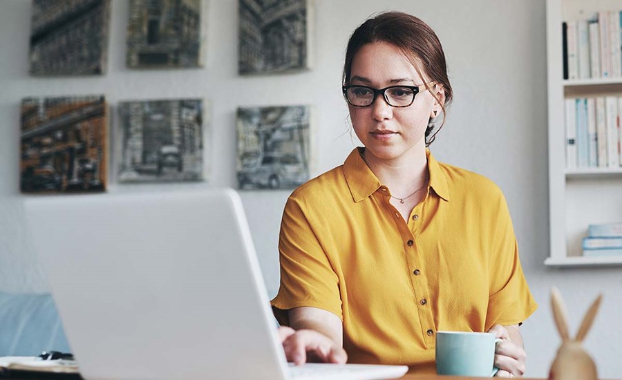 Dame med kaffekopp sitter og jobber på en PC, til illustrasjon for eFaktura