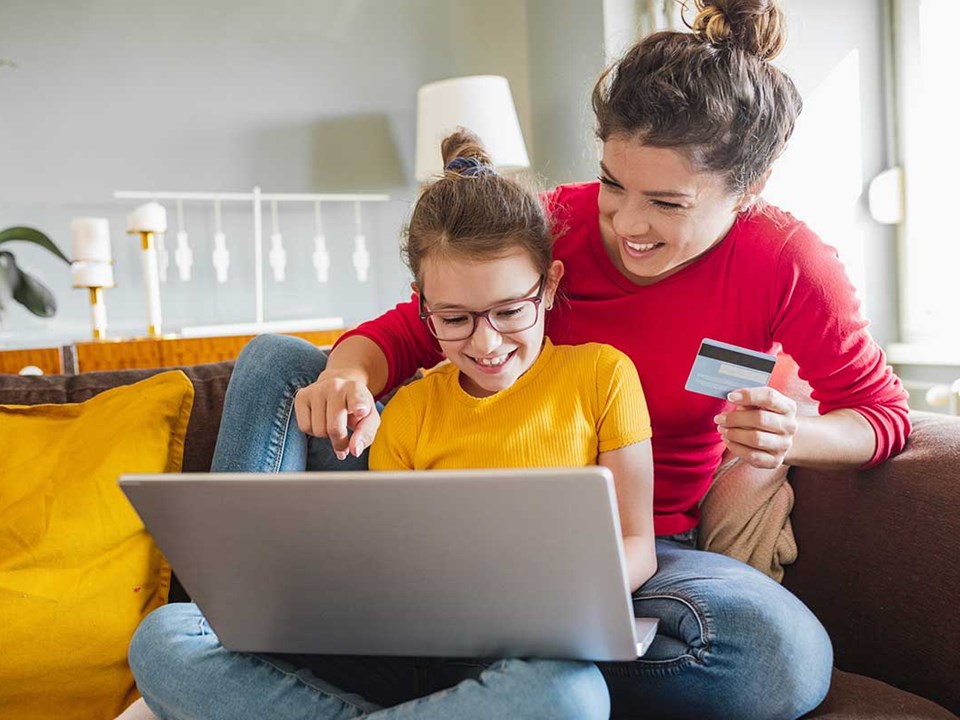 Mor og barn ser på pc med bankkort i handa, til illustrasjon og barn og penger