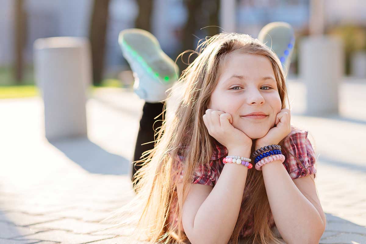 Jente ligger ute på brosteiner og smiler, til illustrasjon for barnekort