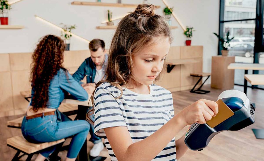 Ung jente betaler med kort på betalingsterminal med to voksne i bakgrunnen, til illustrasjon for barn, penger og økonomi