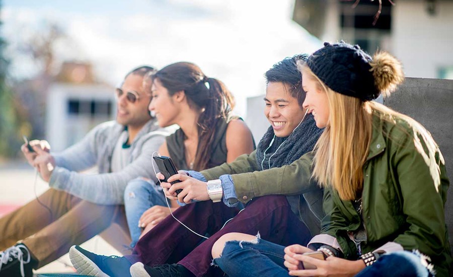 Ungdommer sitter på bakken og ser på mobilene sammen, til illustrasjon for bank for barn og ungdom