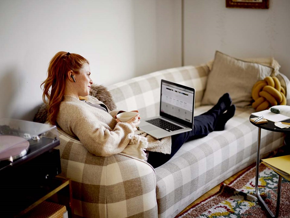jente sitter i sofaen og ser på pc - illustrasjon til trygg kortbruk