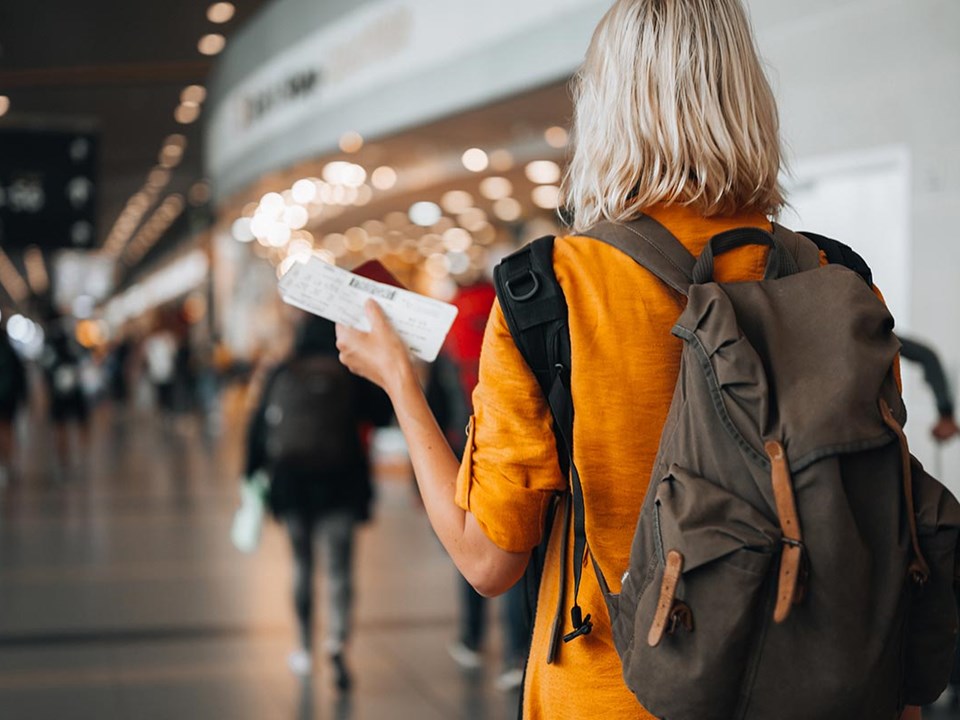 Dame med sekk og holder en flybillett i hånda på en flyplass, til illustrasjon for bankkort