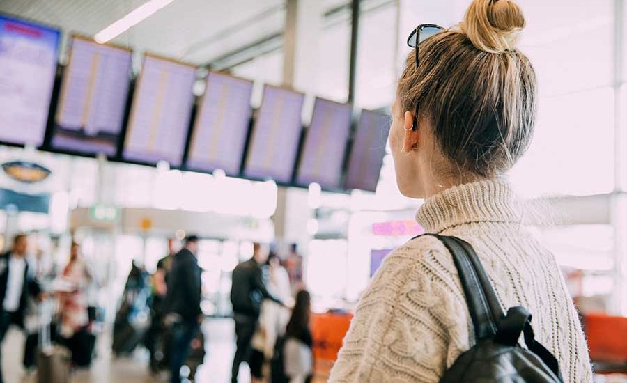 Ung kvinne ser på flyavganger timeplan, til illustrasjon for kredittkort og reiseforsikring