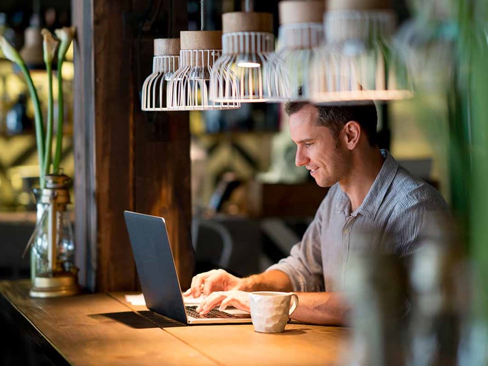 Mann sitter på cafe og ser på laptop, til illustrasjon for mobil-og nettbank